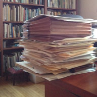 Tall pile of papers on edge of desk